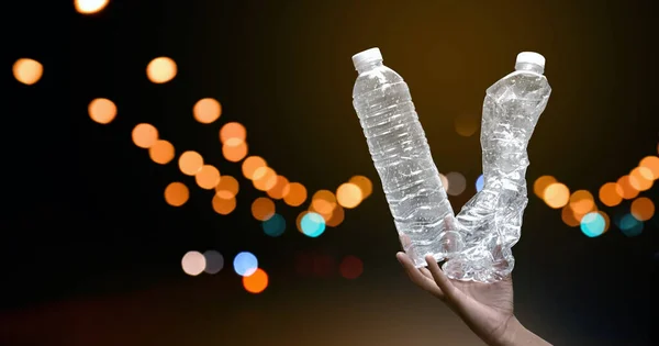 Transparent plastic bottles holding in hand with street bokeh light at night background, concept for do not throw or drop drinking water plastic bottles down to the street to save our environment.
