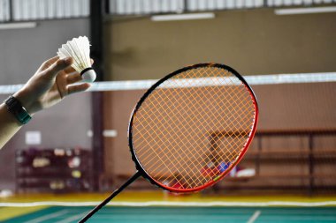 Badminton raketi, badminton oyuncusunun elinde, kapalı badminton kortunda, yumuşak ve seçici bir odak noktası var..