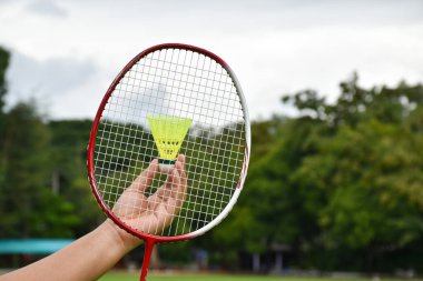 Badminton raketi ve badminton mekik horozları açık havada oynamak için el ele tutuşuyor. Yumuşak ve seçici bir şekilde tellere ve raketlere odaklanıyor. Açık havada etkinlik kavramı..