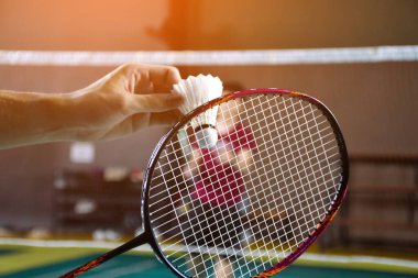 Erkekler tek badminton oyuncusu raketi ve beyaz kremalı mekikçiyi sahanın diğer tarafına sunmadan önce ağların önünde tutuyor, yumuşak ve seçici bir şekilde..