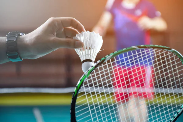 Men single badminton player holds racket and white cream shuttlecock in front of the net before serving it to another side of the court, soft and selective focus.