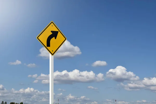 Traffic sign; right arrow curve sign on white pole by the main road with blue sky background, soft and selective focus.