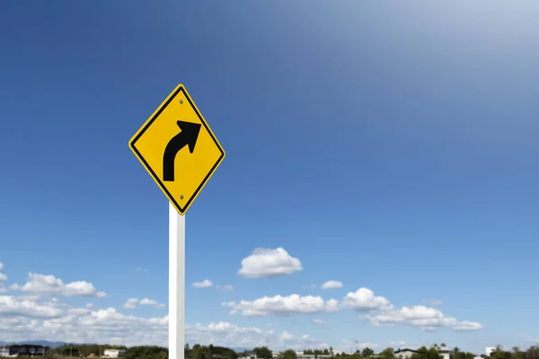 Traffic sign; right arrow curve sign on white pole by the main road with blue sky background, soft and selective focus.