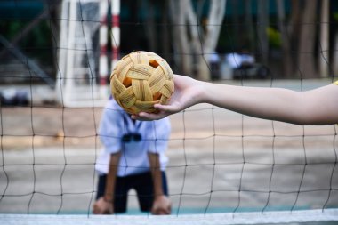 Sepak takraw topu, Güneydoğu Asya ülkeleri geleneksel sporu, genç Asyalı bayan sepak takraw oyuncunun elinde, kalenin önüne atmadan önce topu başka bir oyuncuya atıyor..