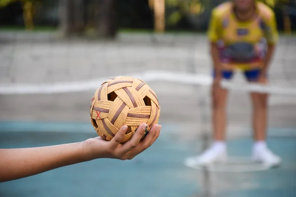 東南アジア諸国の伝統的なスポーツであるセパク タクローボールは 若いアジアの女性の手を握ってネットの前でタクロー選手を奪い それを別のプレーヤーに投げつけてネット上でキックする — ストック写真