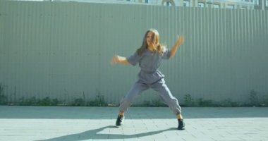 Dans eden kız mutlu ritmik bir şekilde, dokulu sokak çitlerine doğru hareket ediyor. Enerjik genç bayan dansçı eğleniyor.