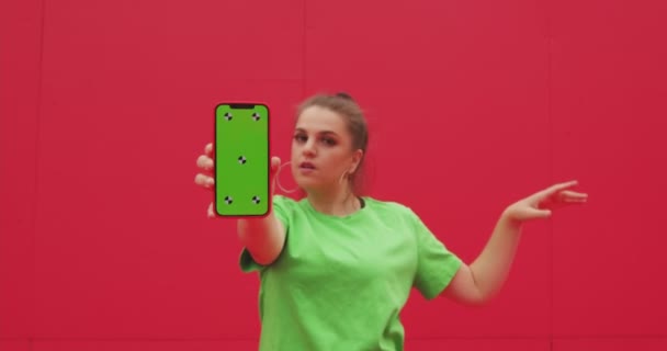 Ευτυχισμένο νεαρό κορίτσι δείχνουν τηλέφωνο με chroma κλειδί πράσινη οθόνη με σημεία εντοπισμού από κόκκινο τοίχο. Διαφήμιση βίντεο αργής κίνησης — Αρχείο Βίντεο