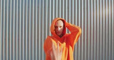 Dans eden genç lgbt kapüşonlu adam sokak arkaplanında dans eden ellerini hareket ettiriyor.