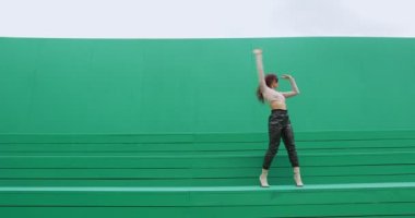 Güneş gözlüklü dans eden kadın yeşil arka planda çağdaş anlamlı danslar sergiliyor. Dansçı kız.