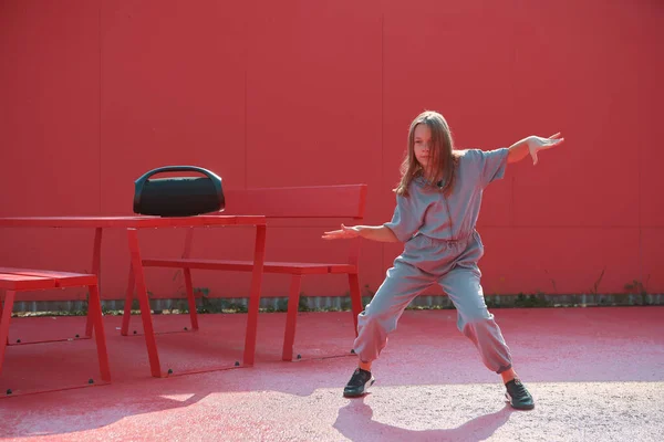 Cool niña bailando con altavoz inalámbrico al aire libre en el exterior sobre fondo rojo. Escuela de baile anuncio —  Fotos de Stock