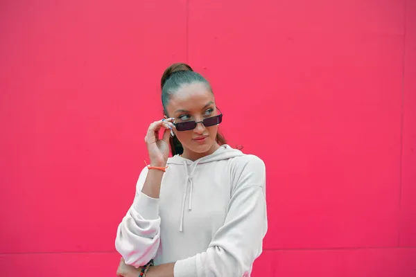 現代若い女の子ブロガーまっすぐスタイリッシュなサングラス見脇にコピースペースのために広告上のピンクの背景 — ストック写真
