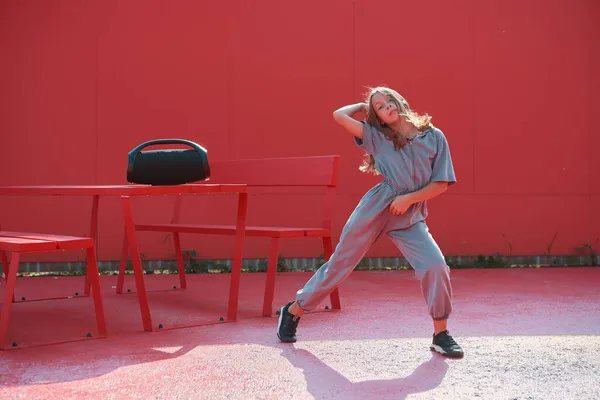 Chica adolescente activa bailando hip hop con altavoz inalámbrico al aire libre fuera sobre fondo rojo. Escuela de baile anuncio —  Fotos de Stock