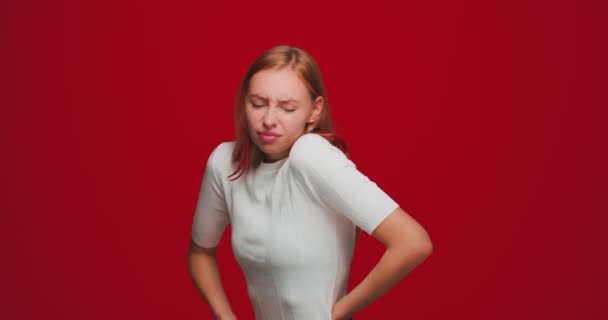 Chica joven con exceso de trabajo que sufre dolor de espalda, espasmos de estilo de vida sedentario, masaje de la columna vertebral dolorida en el fondo del estudio rojo — Vídeo de stock