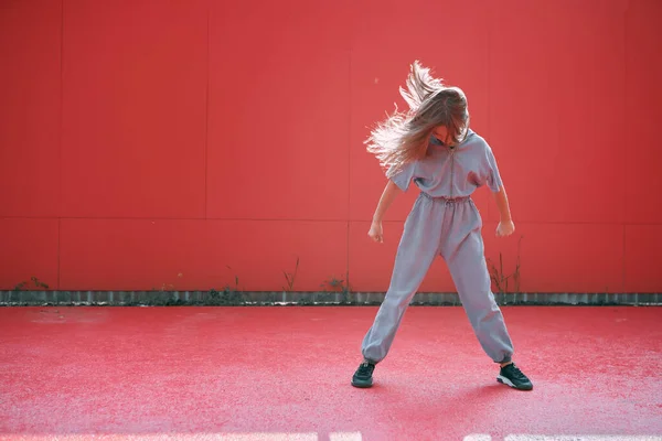 Elegante chica adolescente activa con pelos largos ondeando con ropa moderna sobre fondo rojo con espacio para la publicidad —  Fotos de Stock