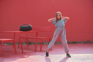 Modern Amerikalı genç kız kablosuz taşınabilir hoparlörüyle sokakta gün ışığında müzik dinlerken poz veriyor.