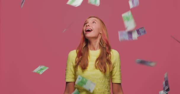 Llueve dinero. Ganadora de la lotería alegre chica rica bajo la lluvia de dinero en efectivo mirando hacia arriba disfrutando de la riqueza en fondo de estudio rosa — Vídeo de stock