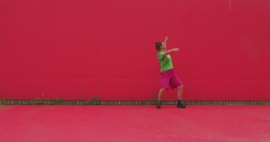 Dans eden mutlu genç kız kırmızı duvara karşı enerjik ve anlamlı dans ediyor. Modern neşeli kadın dansçı. Güzel hareket.