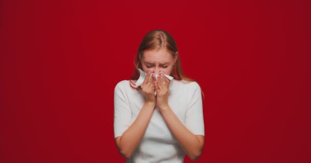 Nemocná mladá dívka kýchání v tkáni, vysmrkání výtok z nosu, utrpení spalin nebo alergie příznaky na červeném pozadí studia — Stock video