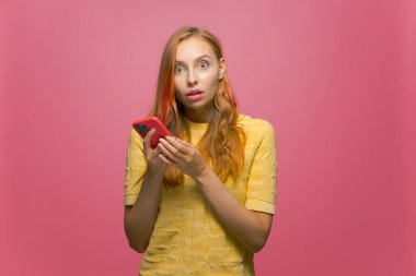 Şok olmuş genç bir kız telefonuyla Pembe Stüdyo arka planında sosyal ağda haber paylaşımı karşısında hayrete düştü.