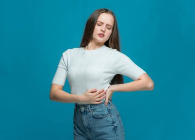 Sağlıksız genç kız bel ağrısı, kas ağrısı aşırı çalışma, mavi stüdyo arka planında sinir sıkışması.