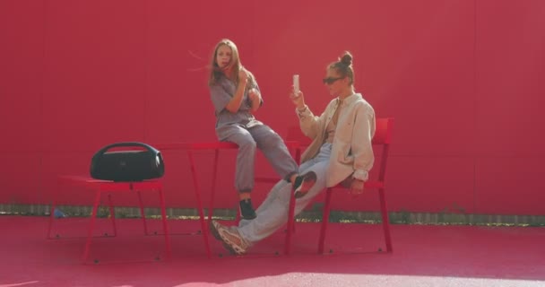 Jóvenes adolescentes escuchan música bailando grabar vídeo en el teléfono para las redes sociales sentado con altavoz de audio en el sol — Vídeo de stock