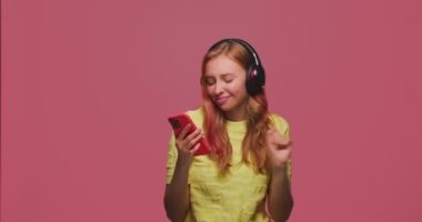 Kablosuz kulaklıklı modern mutlu genç kız dans ediyor, cep telefonu uygulamalarında disko müziği dinlemenin tadını çıkarıyor.
