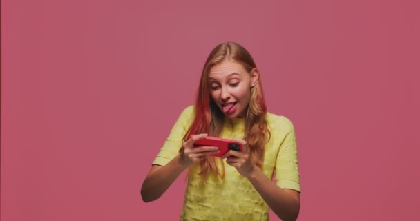 Συγκεντρωμένη νεαρή κοπέλα παίζουν βιντεοπαιχνίδι στο τηλέφωνο, να απολαύσετε gameplay σε αγώνες, διασκεδάζοντας. Εφαρμογή ψυχαγωγίας για κινητά — Αρχείο Βίντεο