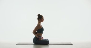 Yoga sınıfı reklamı. Fit sıska genç kız nilüfer çiçeğinde oturur, sırtüstü uzanır, beyaz stüdyoda tepeden tırnağa kıvrılır.