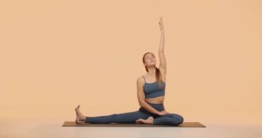 Pilates egzersizi. Genç, esnek bir kız egzersiz yapıyor. Stüdyoda spor minderinin üzerinde bacaklarını ve bacaklarını açıyor.