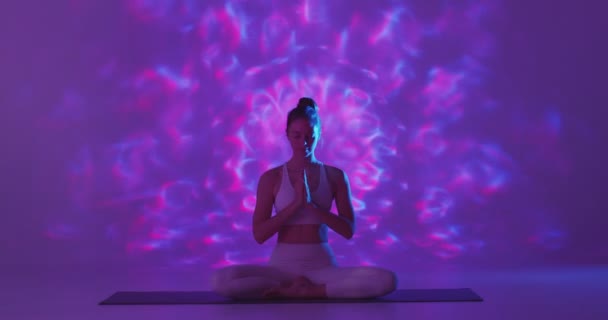 Femeia practică yoga și meditația stând în poziția de lotus, întinzându-se pe fundal violet cu model de aură — Videoclip de stoc