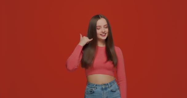 Llámame gesto. Chica joven coqueteando, sonriendo, mostrando el teléfono a mano, ofrecer comunicación sobre fondo naranja — Vídeos de Stock