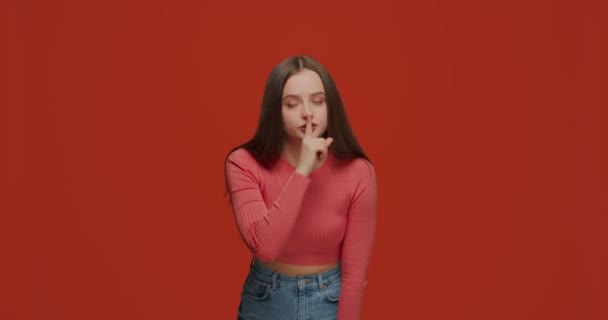 Hezká dívka s ukazováčkem na rtech dělá gesto mlčení, tiše prosí, aby udržela tajemství na oranžovém pozadí — Stock video