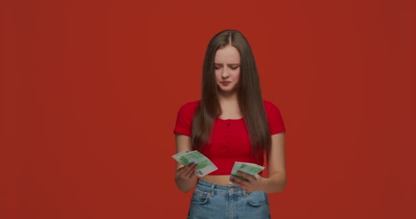 Brist på pengar. Missnöjd ledsen ung flicka räkna kontanter känner stress på orange studio bakgrund. Begreppet fattigdom. — Stockvideo