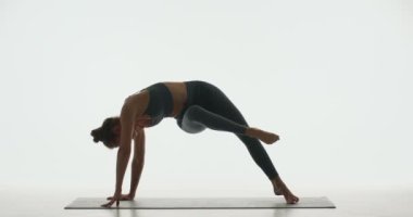 Oldukça esnek bir genç kız yoga yapıyor ya da pilates yapıyor. Omurga sağlığı için beyaz arka planda Vahşi Şey Pozu veriyor.