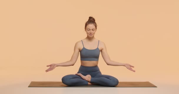 Egy fiatal nő jógázik a stúdióban, kezet hajtogat Namastéban, lótuszban ülve, meditációért pózol. Egészséges életmód