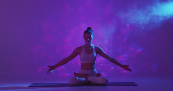 Yoga, méditation pratique ésotérique spirituelle. Fille assise dans la pose de lotus levant les mains, méditant dans la lumière pourpre néon — Video