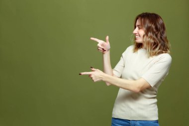 Mutlu genç kadın sol parmağı işaret ediyor. Gülümseyen kız yeni ürün gösteriyor, yeşil arka planda reklam indirimi