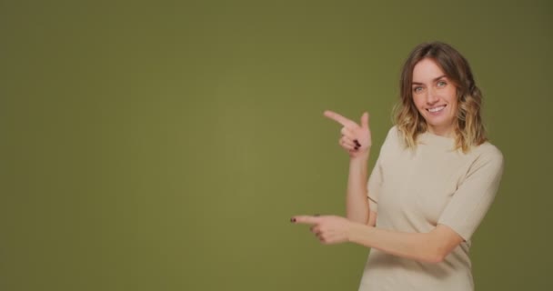 ¡Mira esto! Sonriente chica bastante joven apuntar a un lado por los dedos en el espacio de copia para la publicidad sobre fondo verde natural — Vídeo de stock