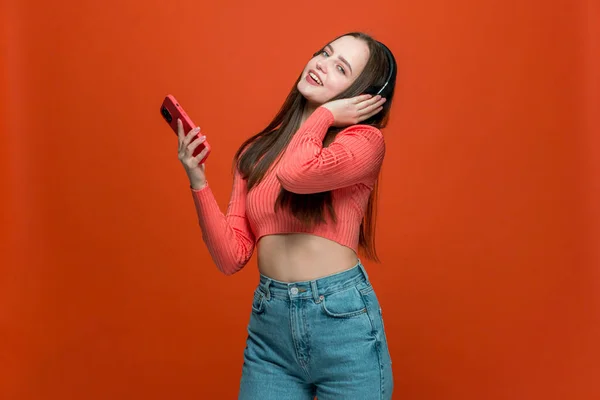 Boldog fiatal modern lány fülhallgató és okostelefon zenét hallgatni élvezi hűvös lejátszási lista narancs háttér — Stock Fotó