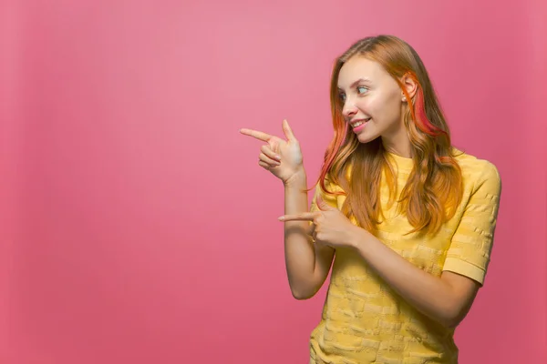 Hermosa joven sonriente señalando los dedos a un lado en el espacio de copia sobre fondo rosa. Promoción, publicidad maqueta — Foto de Stock