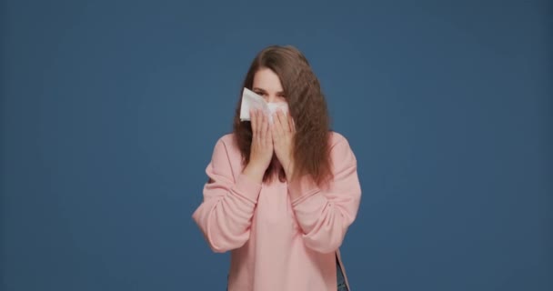 Симптомы гриппа. Больная молодая девушка чихает в салфетке, чувствует себя нездоровым, страдает от гриппа в воздухе на синем фоне — стоковое видео
