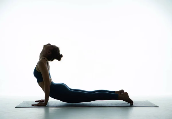 在白工作室里，灵活的年轻女孩练习瑜伽，做眼镜蛇姿势，伸展身体肌肉以保持健康 — 图库照片