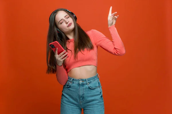 Moderna chica joven adolescente con estilo en auriculares disfrutando de ritmo de música impresionante, bailando con la mano levantada sosteniendo el teléfono inteligente —  Fotos de Stock