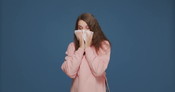 Doente menina alérgica soprando corrimento nasal no tecido. Mulher doente sofre de gripe frio ou sintomas de alergia em fundo azul — Vídeo de Stock