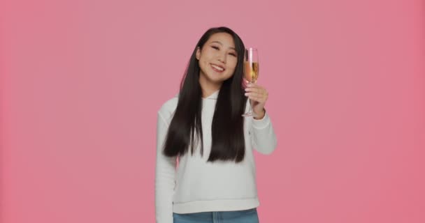 明けましておめでとうございます。若いアジアの女の子を笑顔最高の願いはピンクのスタジオの背景にシャンパンを飲む.休日パーティー — ストック動画