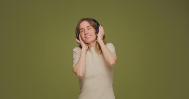 Happy young girl dj listening music with headphones, enjoying sound, dancing on green studio background — Stock Video