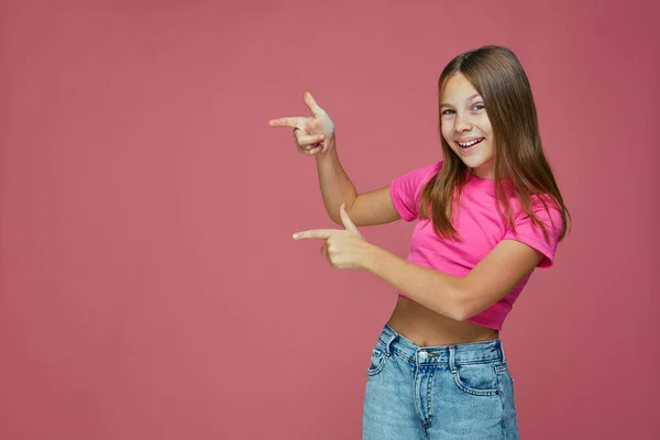 Glückliches kleines Mädchen, das mit dem Finger auf Kopierraum zeigt, Werbung für Kinderprodukte oder Babyservice auf rosa Hintergrund — Stockfoto