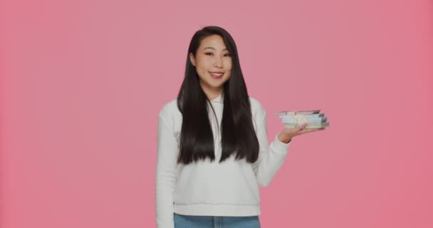 Mosolygó gazdag fiatal ázsiai lány kezében, és rámutatva dollár halom készpénz, pénz megtakarítás, betét. Bankok és befektetések — Stock videók