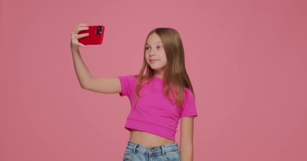 かなり子供の女の子ブロガーは、ソーシャルネットワークのために自撮りを取ります,カメラと楽しみを持っています,ピンクの背景に写真のためにポーズ — ストック動画
