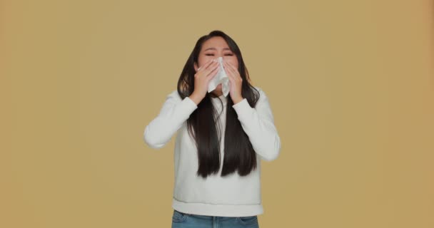 Doente jovem asiático menina sofrer frio ou alergia, sentindo-se mal, soprando esfregando corrimento nariz por guardanapo no fundo amarelo — Vídeo de Stock